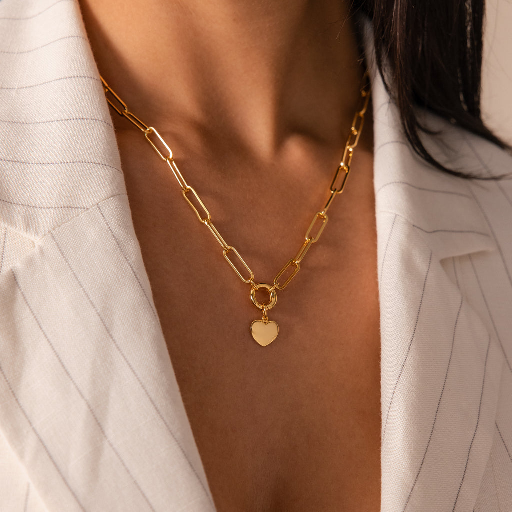 A woman wears the Paperclip Heart Charm Necklace, featuring a heart pendant, over a white pinstripe blazer.
