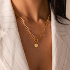 A woman wears the Paperclip Heart Charm Necklace, featuring a heart pendant, over a white pinstripe blazer.