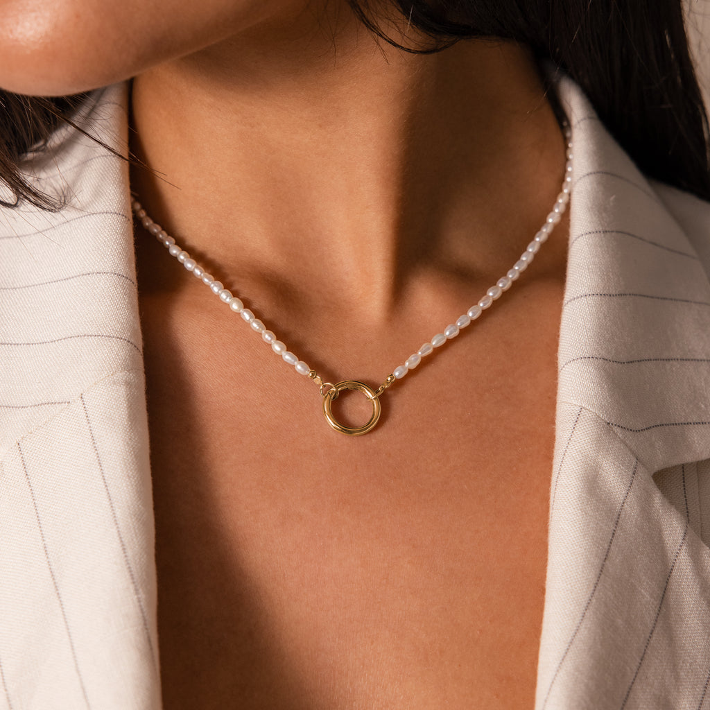 Close-up of a woman wearing our Pearl Chain Clasp Necklace, featuring a gold ring pendant, styled with a cream pinstripe blazer.
