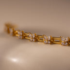 The Mariposa Link Bracelet, a gold piece adorned with diamond settings, rests elegantly on a smooth beige surface—a stunning choice for feminine jewelry.