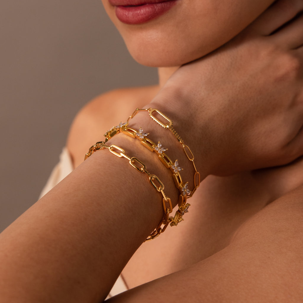 A woman's hand near her face showcases the Mariposa Link Bracelet—a gold butterfly design paired with two elegant gold bracelets for a refined, feminine look.