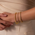 A person wearing an elegant Heart Tennis Bracelet and cream-colored clothing rests their hand on their hip.