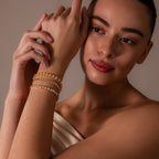A woman with a soft expression poses with one arm raised, showcasing the Diamond Heart Rope Bracelet along with gold bracelets.