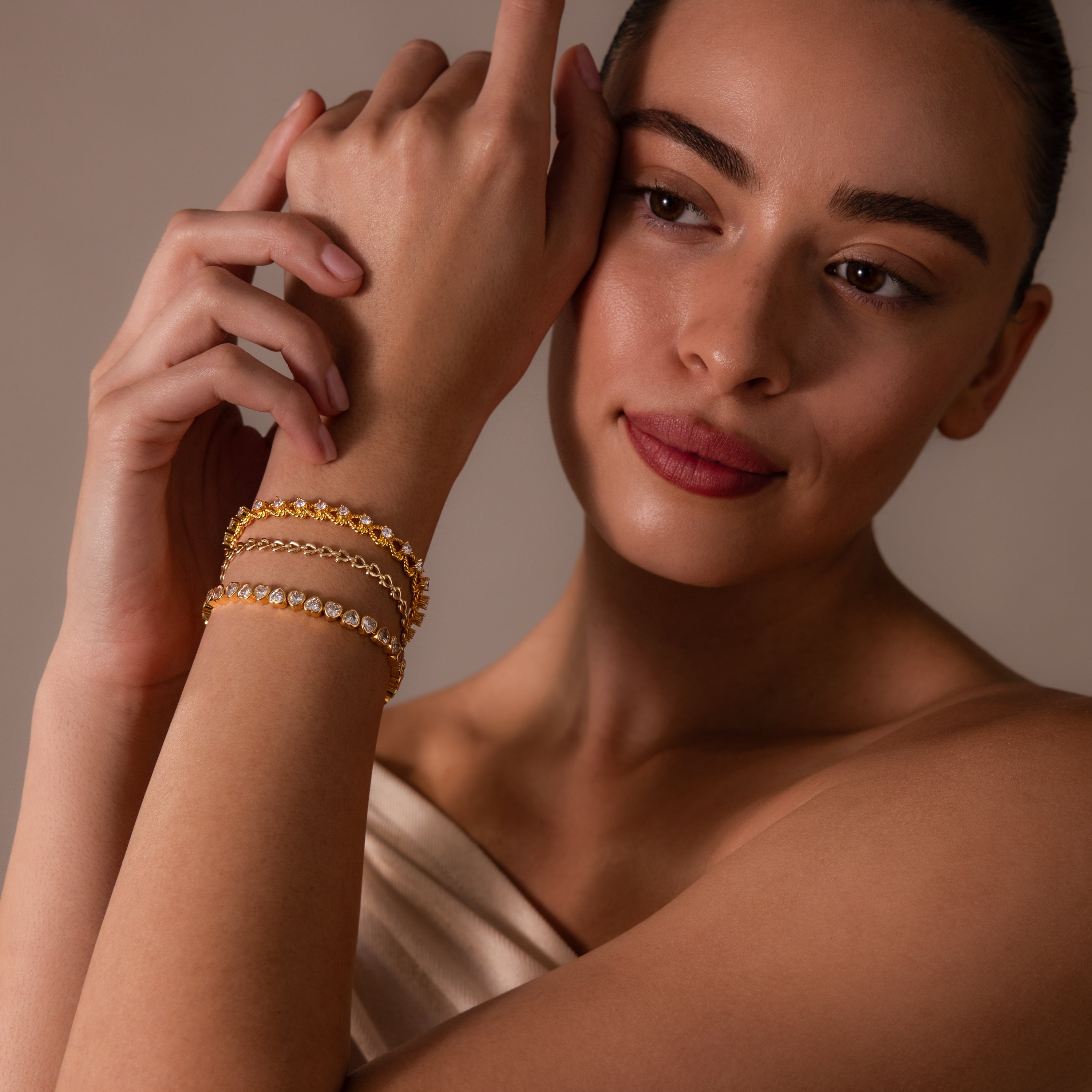 A woman wearing an off-shoulder top elegantly showcases the Heart Tennis Bracelet with heart-shaped stones on her wrist, glancing to the side with a gentle smile.