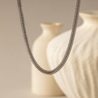 hick Mesh Chain Necklace in silver floats against a soft neutral backdrop. The lighting enhances the tightly interlocked mesh links, showcasing the necklace’s uniform weave
