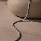 A modern jewelry piece, the Bold Snake Chain Necklace rests on a smooth beige surface with soft shadows—perfect as a sleek layering necklace.