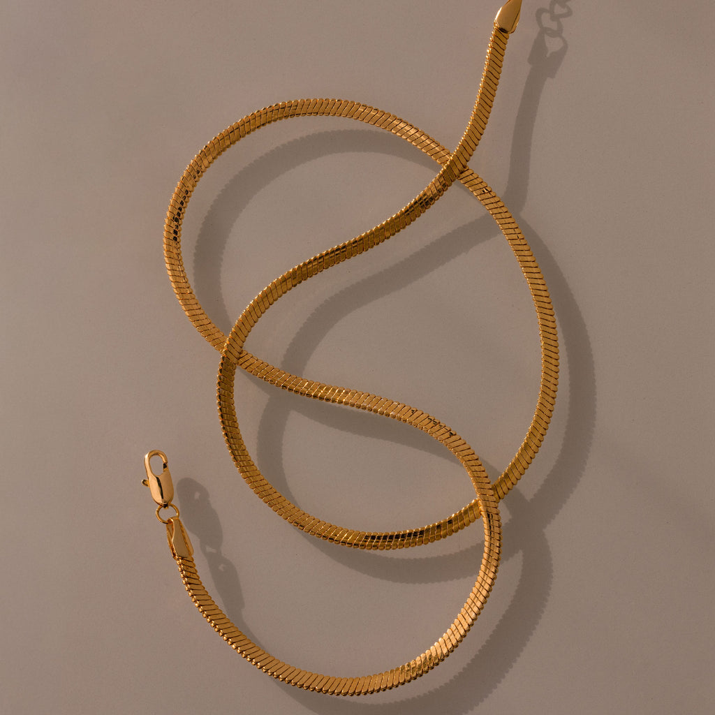 The Bold Snake Chain Necklace in 18K Gold features a lobster clasp and modern design, shown in an S shape on a neutral background—perfect for layering.