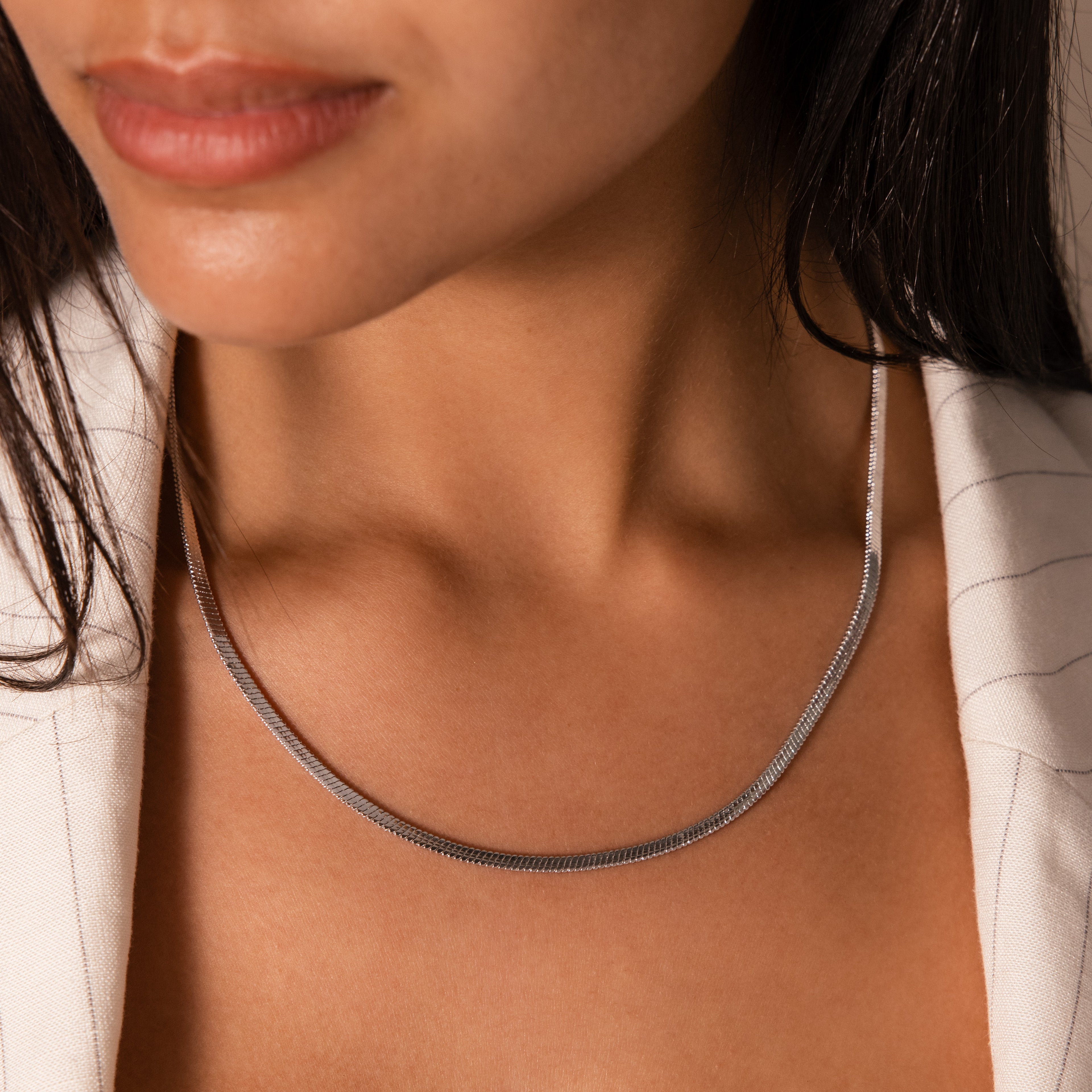 A woman wearing the Twisted Snake Chain Necklace in Silver, paired with a white pinstripe blazer, embodies modern jewelry elegance.