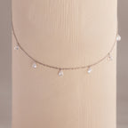 Diamond teardrop station necklace in silver draped around a textured cylindrical display in soft lighting.