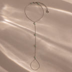 Jade Hand Chain Bracelet in Silver featuring small pale green jade beads, shown on a beige surface with soft, dappled light.