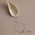 The Jade Hand Chain Bracelet in Silver is displayed on a cream-colored seashell, featuring a delicate silver chain adorned with jade beads.