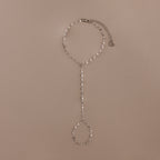 The Sparkle Hand Chain Bracelet in Silver features mirror cut links, a linked finger loop, and an adjustable clasp, beautifully displayed on a beige background.