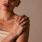 A woman in a strapless top wears the Sparkle Hand Chain Bracelet featuring delicate mirror cut links, her hands gently crossed.