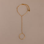 The Sparkle Hand Chain Bracelet in 18K Gold features mirror-cut links and an adjustable clasp, shown on a beige background.