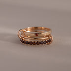 The Triple Linked Garnet Ring Set features two stacked gold rings: one with a single small red stone and another eternity band adorned with a row of small red garnet gemstones.