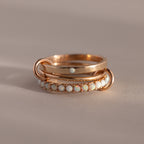 The Triple Linked Opal Ring Set features elegant gold rings with opal stones, beautifully displayed on a neutral beige background.