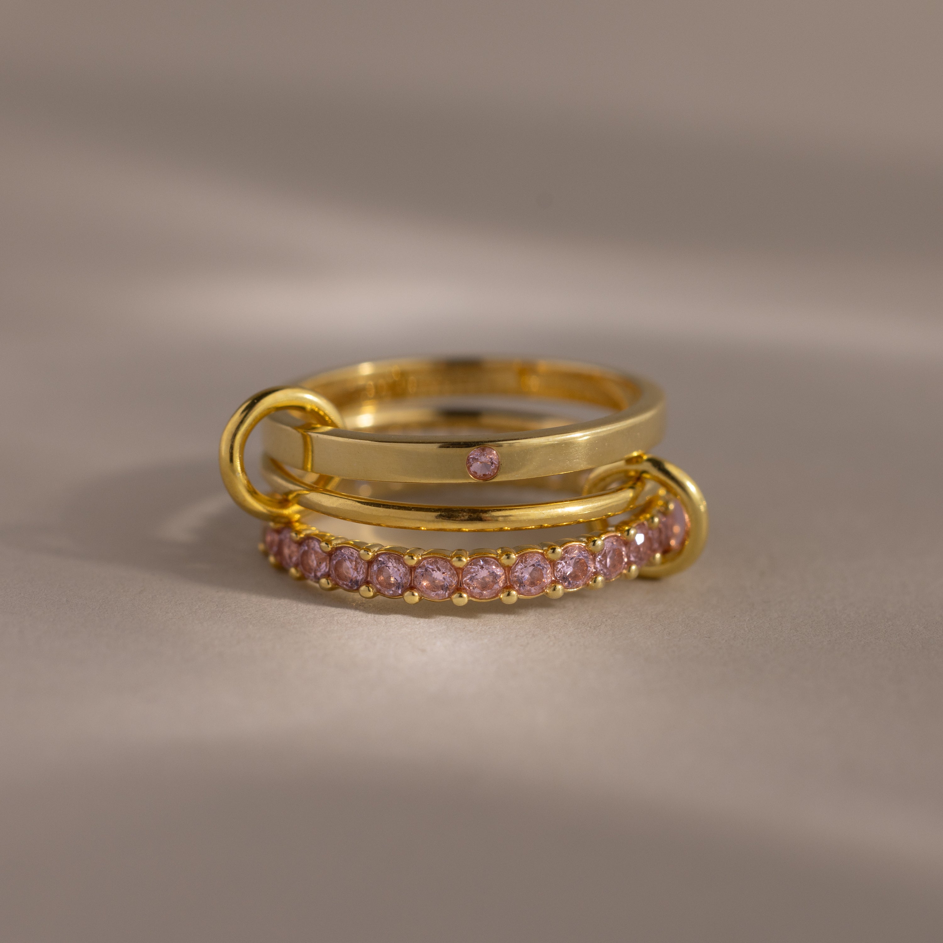 The Triple Linked Pink Tourmaline Ring Set features three gold rings, including two with pink tourmaline gemstones, elegantly stacked for a timeless and delicate look.