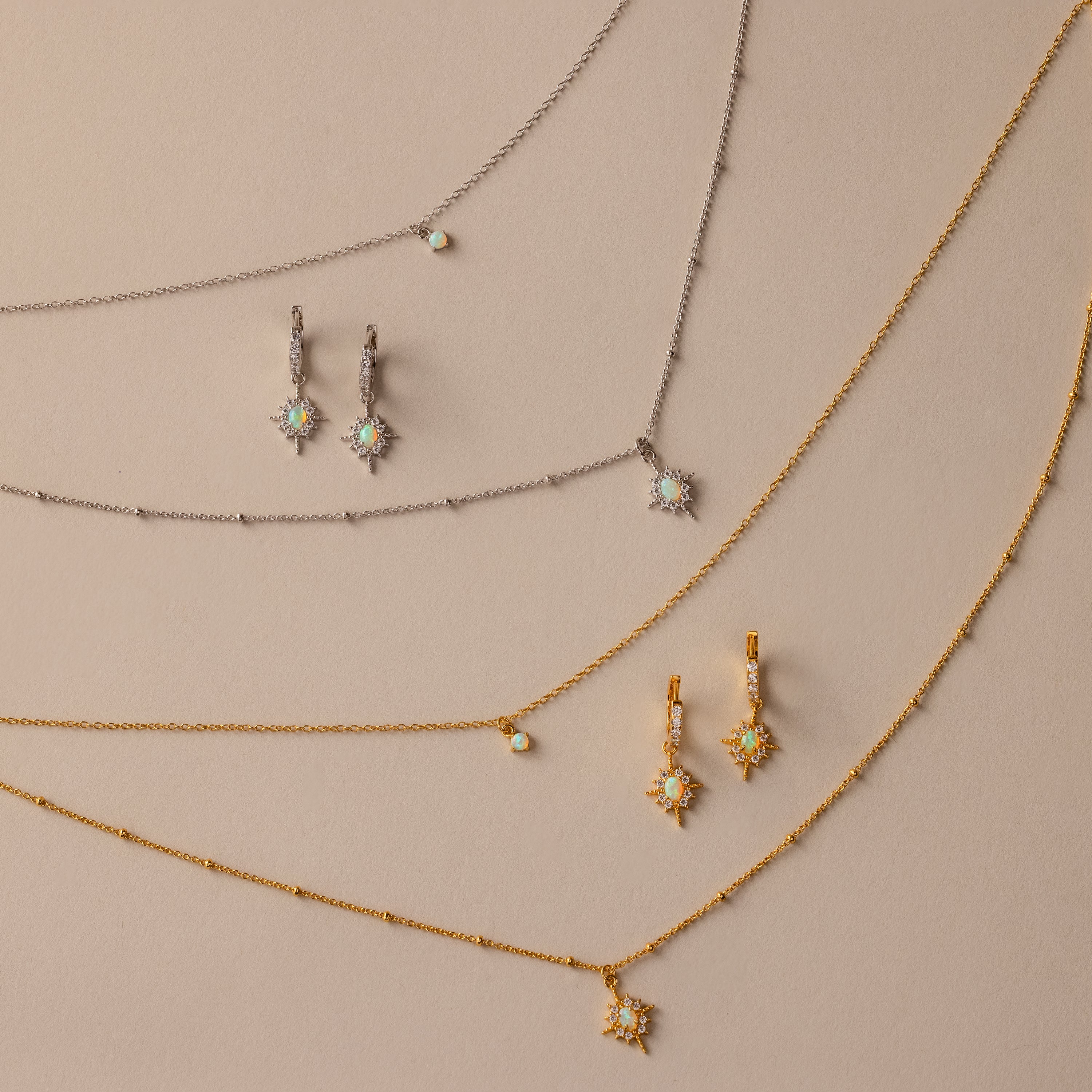 The Opal Star Necklace & Earrings Set in 18K Gold, featuring gold and silver star designs, is beautifully displayed on a beige background.