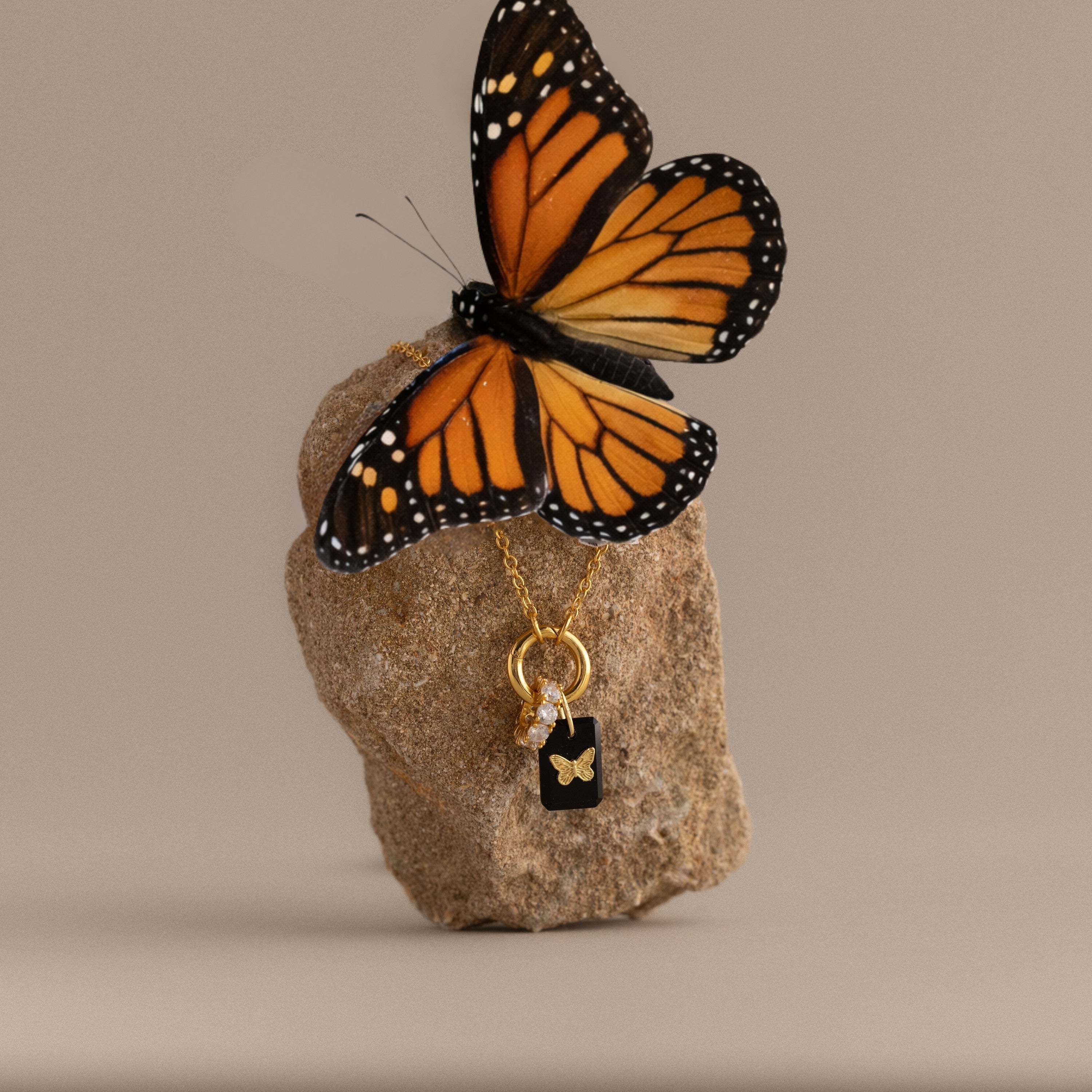 A monarch butterfly on a rock showcases the Onyx Butterfly Charm, a gold necklace ideal for nature lovers and butterfly jewelry enthusiasts.