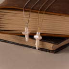 Two Baroque Pearl Cross Necklaces in Silver with minimalist chains rest gracefully against the pages of two stacked books.