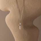 The Baroque Pearl Cross Necklace in Silver, featuring a minimalist chain and freshwater pearl cross pendant, is displayed on a textured beige mannequin bust, adding elegant style to any outfit.