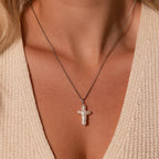 A close-up of a woman wearing the Baroque Pearl Cross Necklace in Silver with a cream knit top, showcasing the elegance of this freshwater pearl accessory.