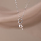 The Cross & Heart Charm Bracelet in Silver is displayed on a soft beige background.