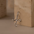 The Infinity Cross Charm in Silver, symbolizing eternal faith, rests against a beige textured stone surface.