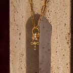 The Infinity Cross Charm in 18K Gold, paired with a paperclip chain and lion charm, is elegantly displayed on a textured stone—a symbol of eternal faith and meaningful style.