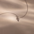 The Vintage Cross Necklace in Silver is a minimalist piece featuring a pavé-finish, diamond-studded cross pendant, shown on a beige textured surface.