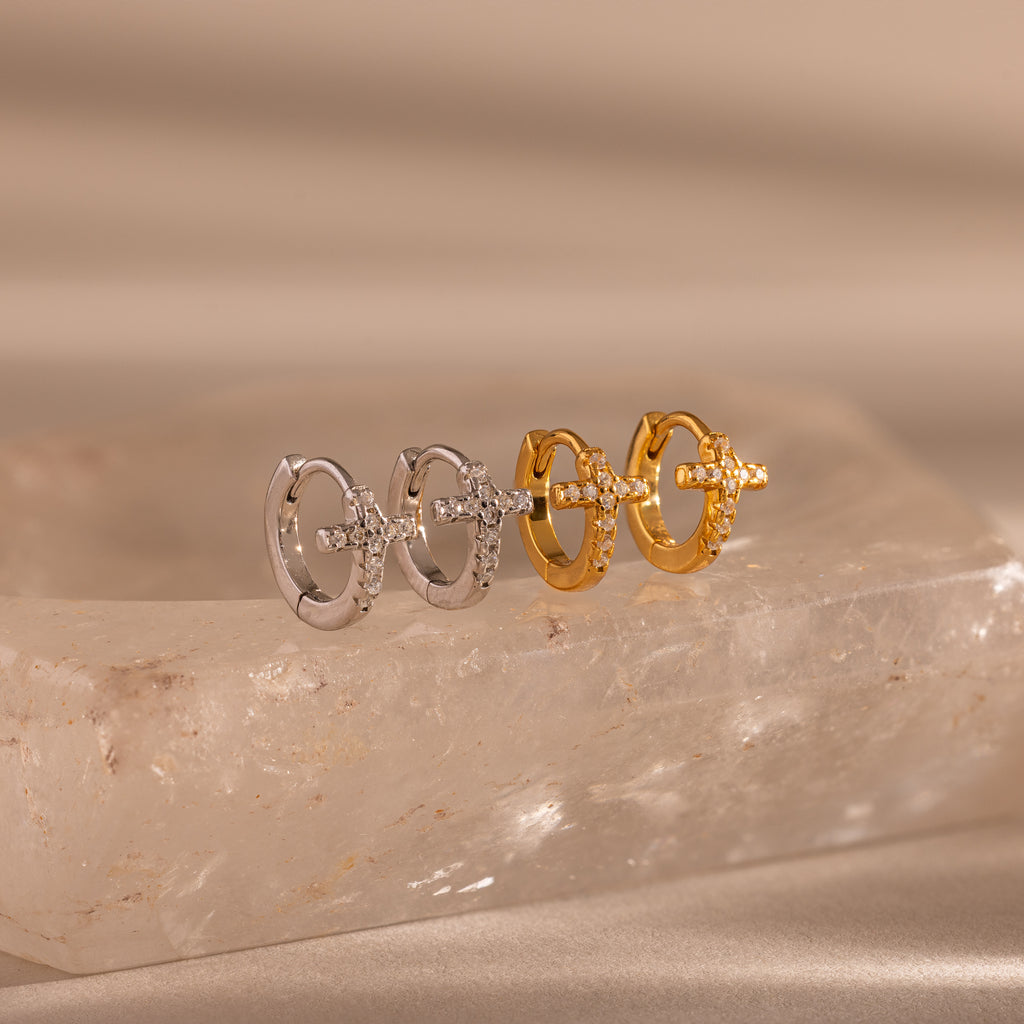 Two pairs of Diamond Cross Huggies, one in silver and one in gold, each featuring pavé stones on the cross charms, displayed on a stone slab.