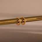 Diamond Cross Huggies in 18K Gold, featuring cross designs and pavé stones, hang on a metallic rod against a neutral background.