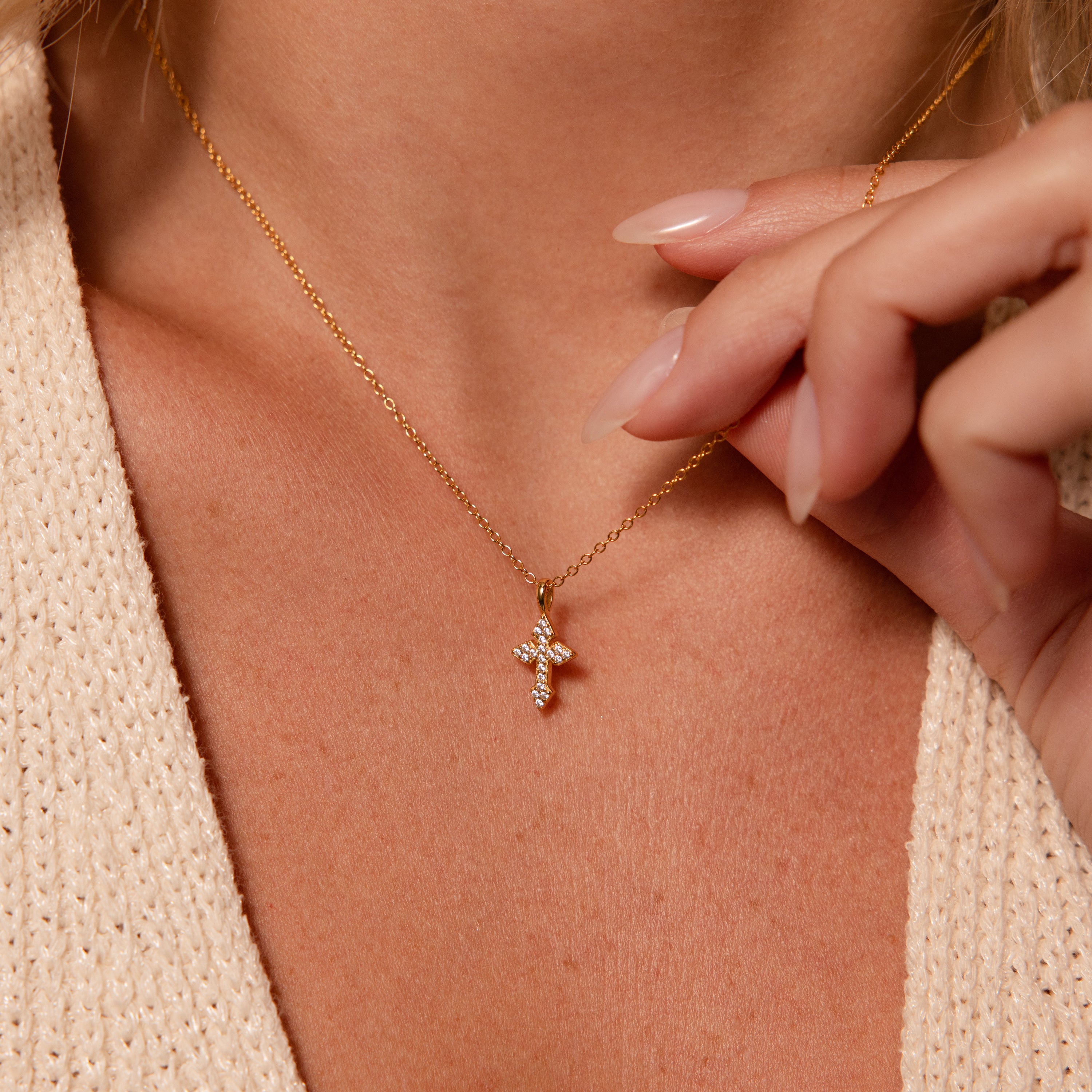 A close-up of a woman wearing the Vintage Cross Necklace with a pavé finish and small diamond pendant as she delicately holds its chain.