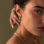 Woman touching her ear, wearing Pearl Heart Beaded Drop Studs in 18K Gold with a pearl necklace against a neutral background—an ideal bridesmaid gift.