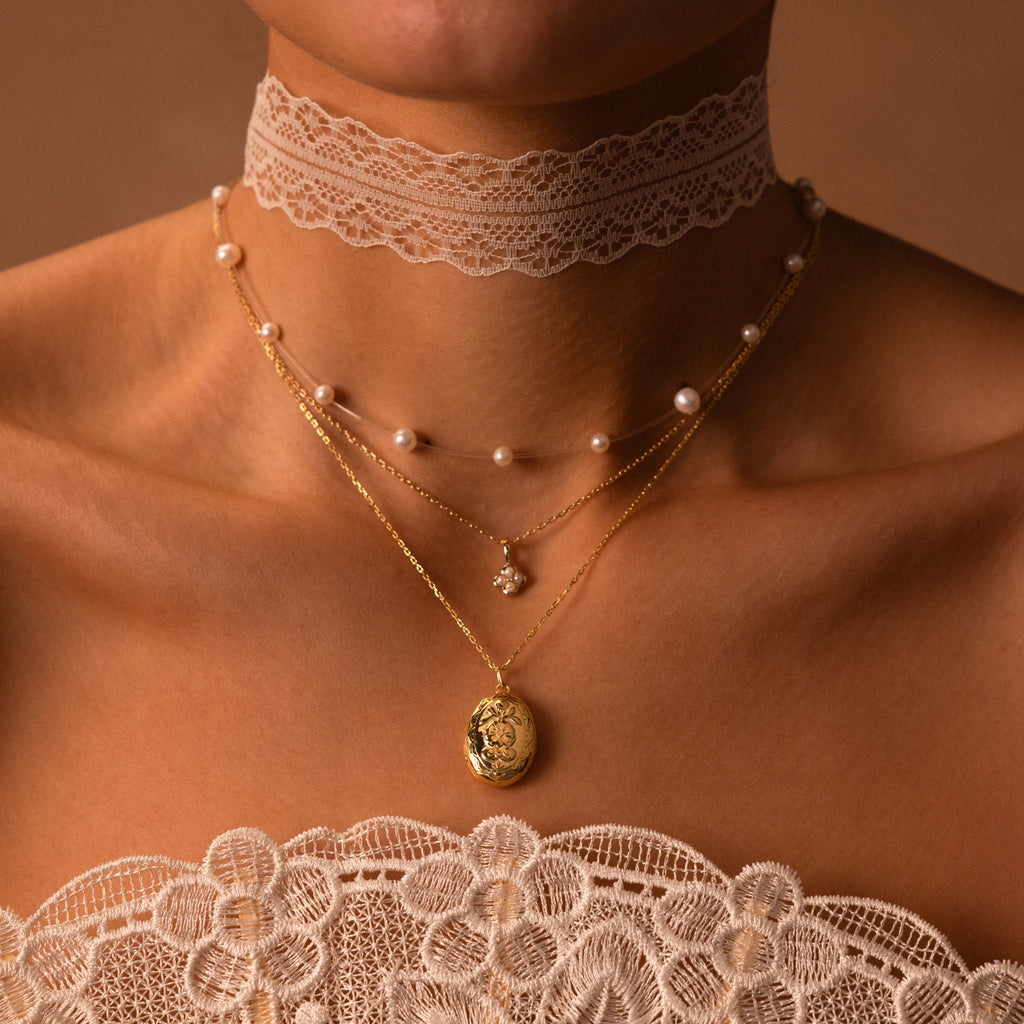 Woman wearing the Floating Pearl Necklace layered with a lace choker and delicate gold necklaces over a lace top, set against a brown background.