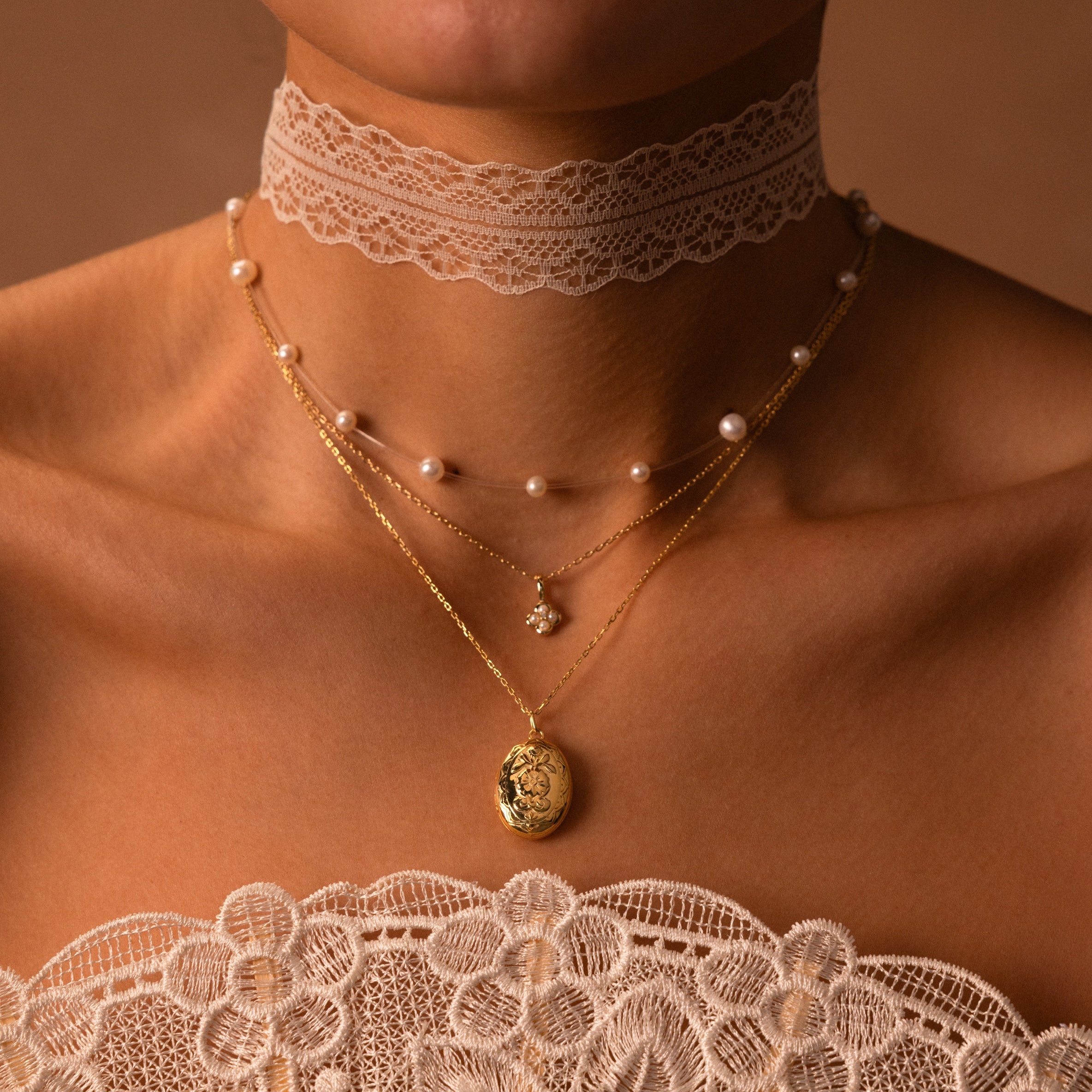 Woman wearing the Floating Pearl Necklace layered with a lace choker and delicate gold necklaces over a lace top, set against a brown background.