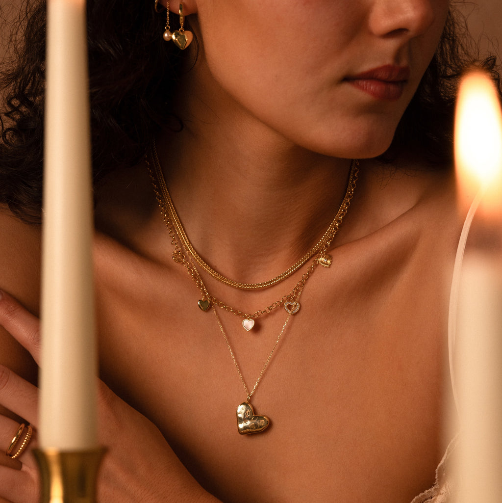 Woman wearing the Organic Heart Locket Necklace and earrings, with candles in the foreground—an elegant display of meaningful keepsake jewelry.