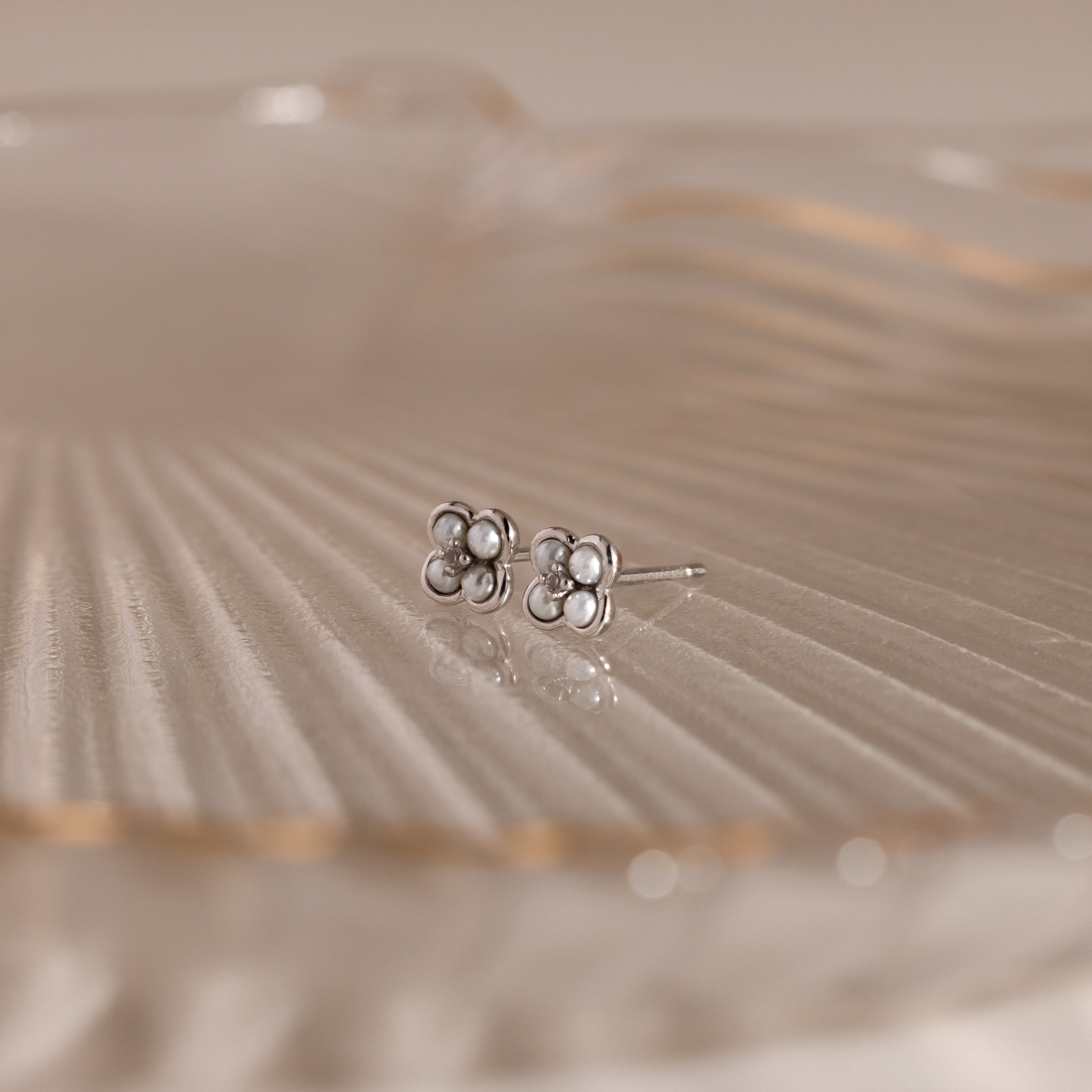 Rounded Pearl Flower Studs in Sterling Silver, featuring small pearls in a floral design, displayed on translucent ribbed glass—an elegant choice for bridesmaid jewelry at any special occasion.