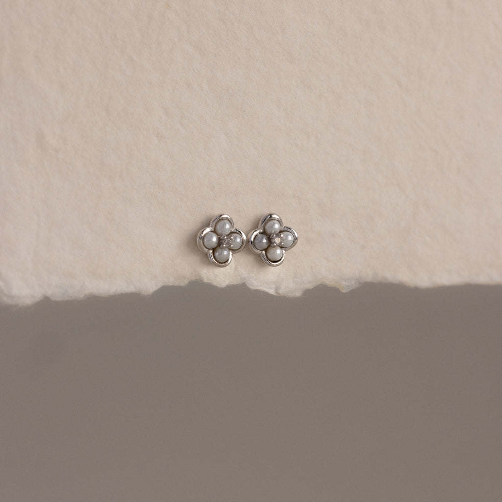The Rounded Pearl Flower Studs in Sterling Silver, featuring pearl-like centers, are displayed on a textured off-white surface—an elegant choice for bridesmaid jewelry.