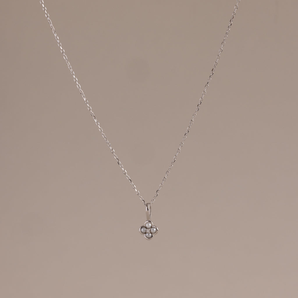 The Rounded Pearl Flower Necklace in Sterling Silver features a delicate chain and a small, three-pearl floral pendant, perfect for everyday layering and adding subtle elegance to any neutral background.