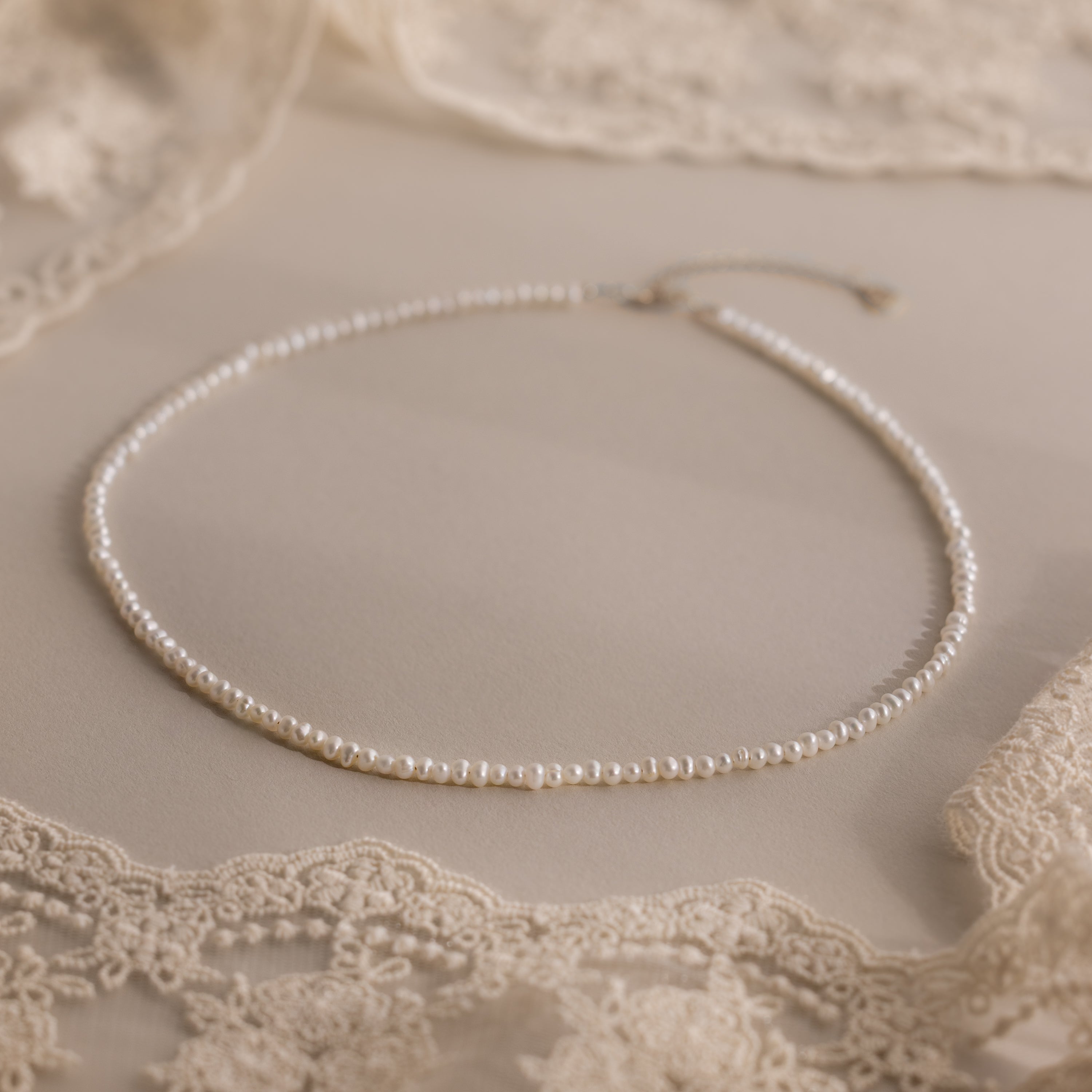 The Summer Pearl Beaded Necklace in Sterling Silver is displayed on a beige lace fabric background, making it the perfect choice for modern pearl jewelry this summer.