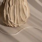 The Summer Pearl Beaded Necklace in Sterling Silver is displayed draped over a textured beige stone, with soft shadows falling across a neutral background for a modern, elegant look.