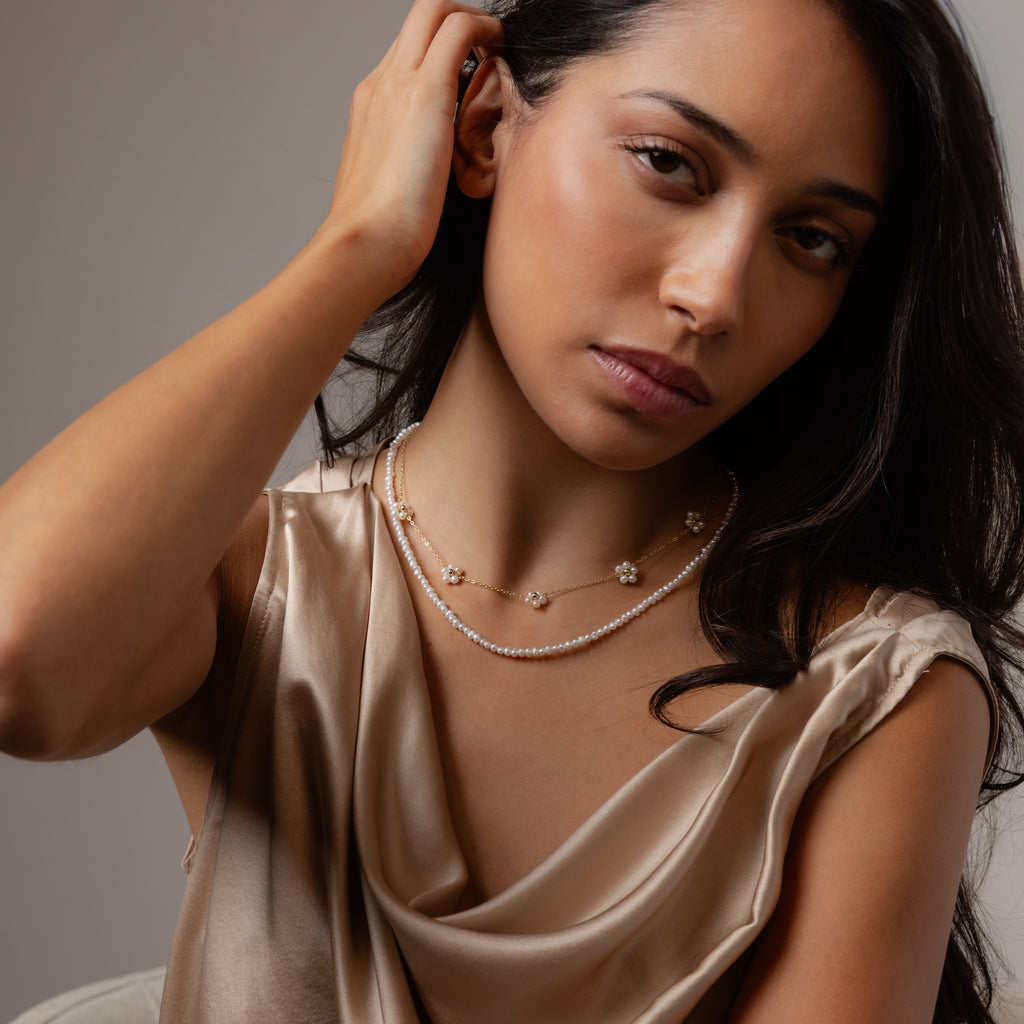 Woman in a satin top wears the Summer Pearl Beaded Necklace in Sterling Silver, styled in layered pearls, as she touches her hair and looks at the camera.