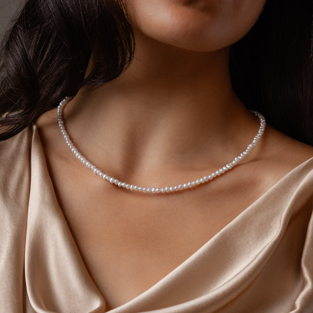 A woman showcases the Summer Pearl Beaded Necklace in Sterling Silver, paired with a champagne satin top that highlights her neck and collarbone.