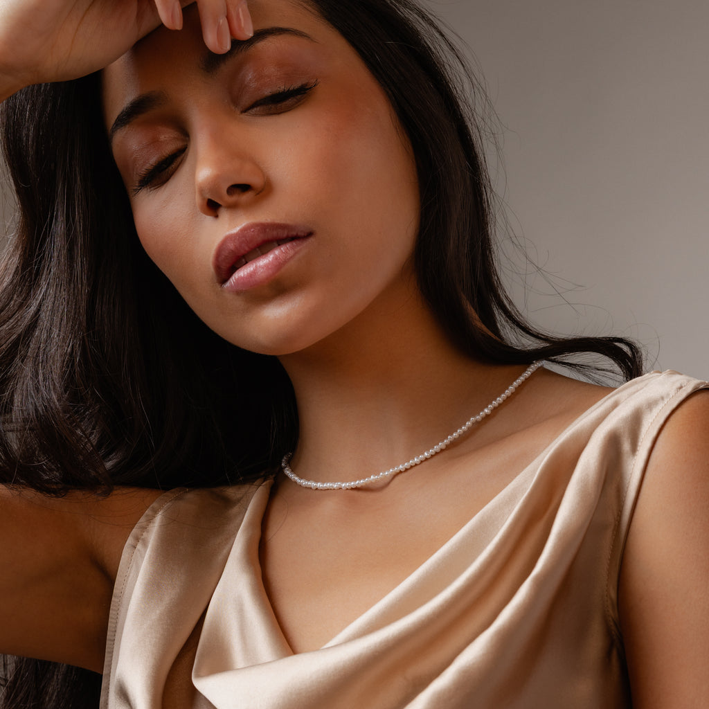Woman with eyes closed wearing the Summer Pearl Beaded Necklace in 18K Gold, styled with a satin dress and posing against a neutral background.