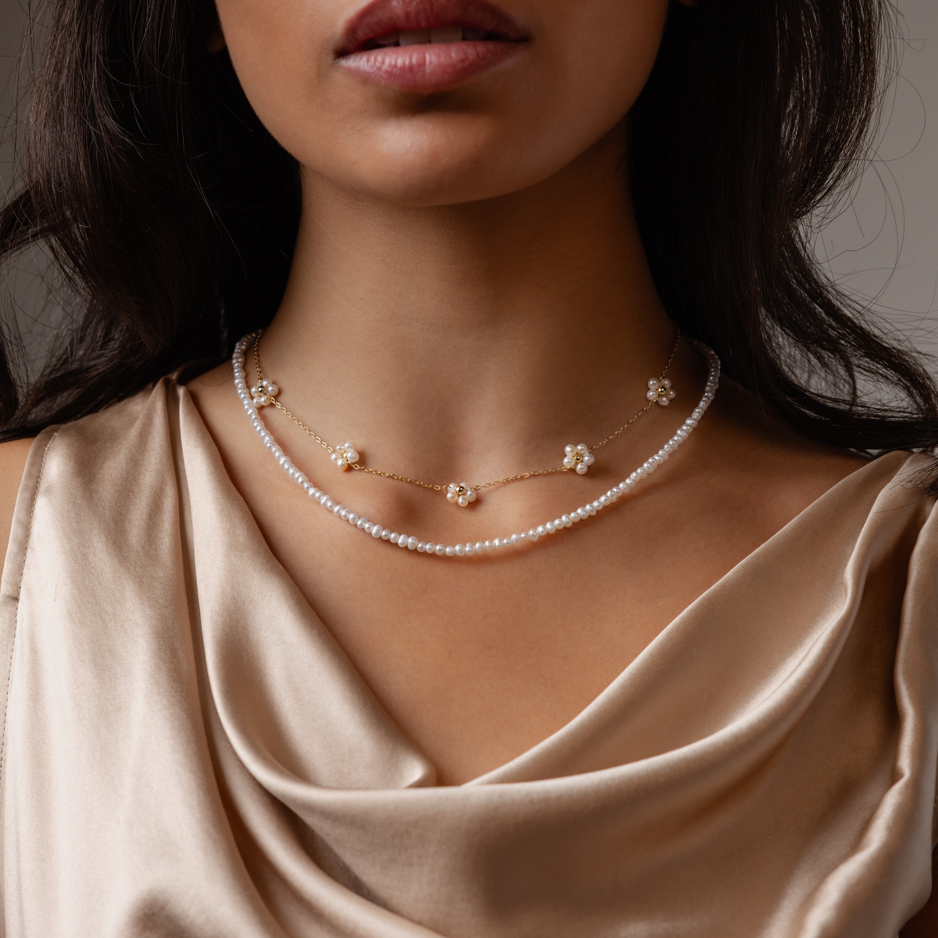 Woman wearing the Summer Pearl Beaded Necklace layered with gold floral pieces and a champagne satin top, showcasing modern pearl jewelry that’s perfect for summer.