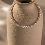 A Venus Pearl Bracelet draped over a textured beige ceramic vase highlights the timeless allure of freshwater pearls.