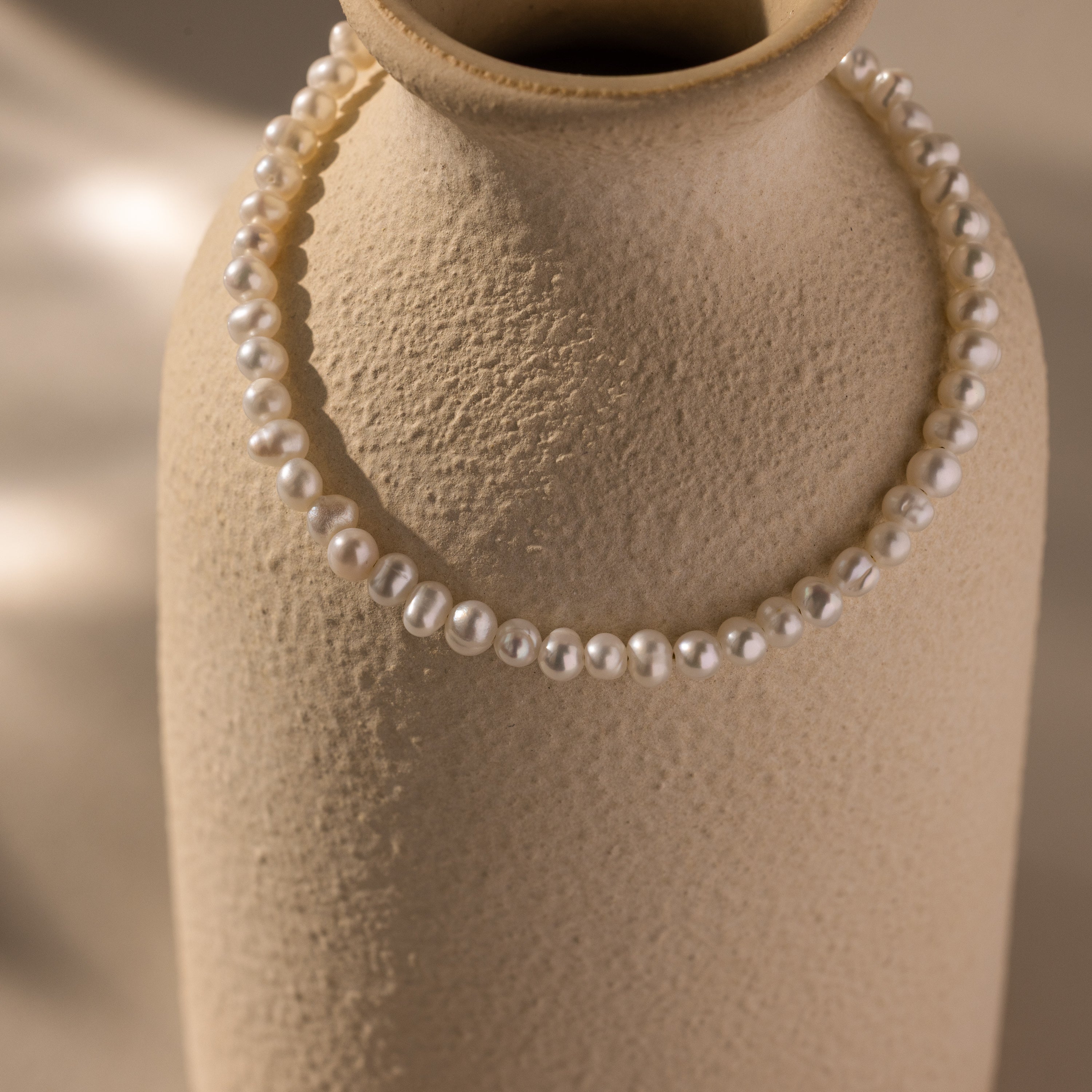 A Venus Pearl Bracelet draped over a textured beige ceramic vase highlights the timeless allure of freshwater pearls.
