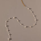 The Floating Pearl Necklace, featuring delicate freshwater pearls and a gold clasp, is arranged in a graceful curve on a beige surface.