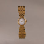 The Brick Link Timepiece is a gold sculptural watch with a round face and bold brick-link bracelet, showcased on a plain, light brown background.